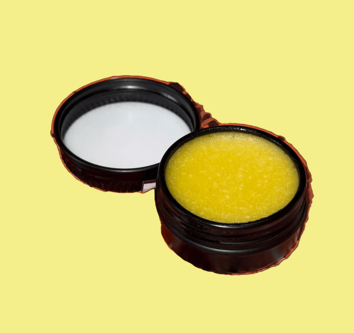 A small round black container shown open, with the lid placed beside it. The container holds a bright yellow balm or cream, photographed on a plain yellow background.