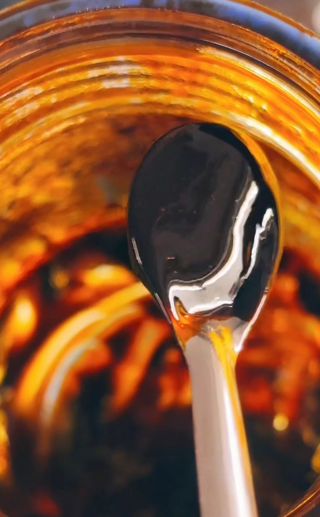 Dark red Cayenne Pepper extract on a metal spoon over a jar filled with cayenne extract.