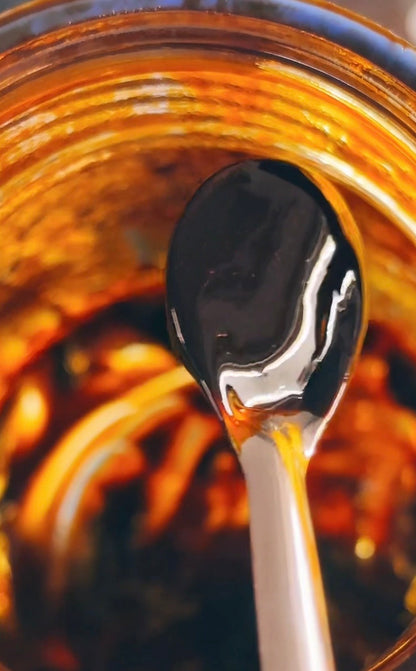 Dark red Cayenne Pepper extract on a metal spoon over a jar filled with cayenne extract.