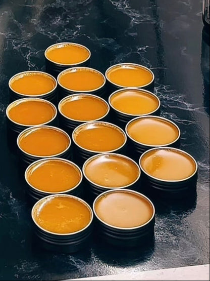 Small round cosmetic tins filled with orange balm mix arranged on a black countertop.